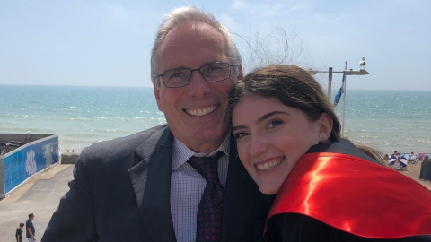 A man in a suit hugs his daughter in her graduation robes.